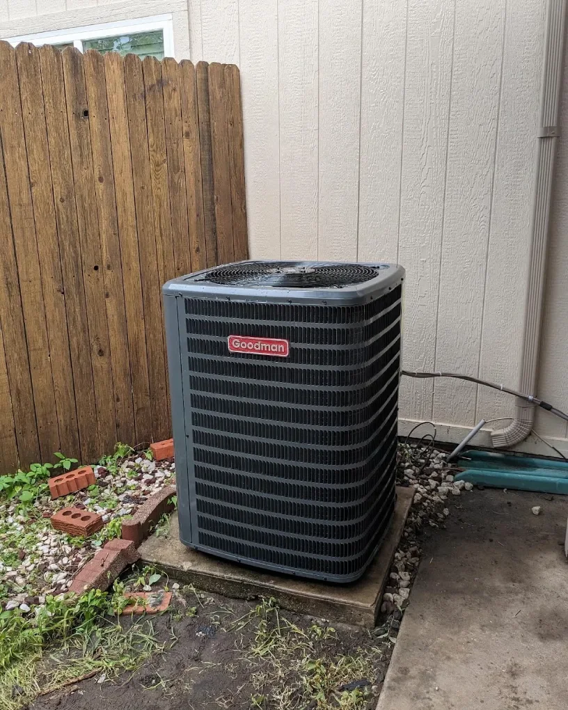 Goodman outdoor air conditioning condenser beside a residential fence and siding