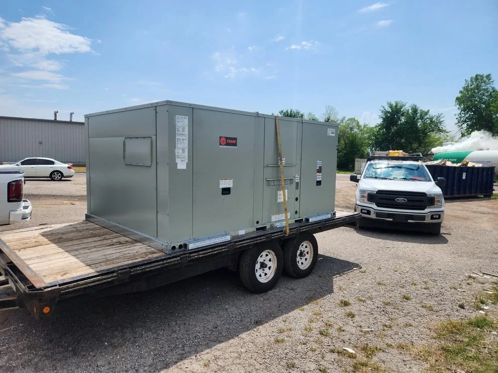 Large Trane packaged HVAC unit secured to a flatbed trailer beside a work truck