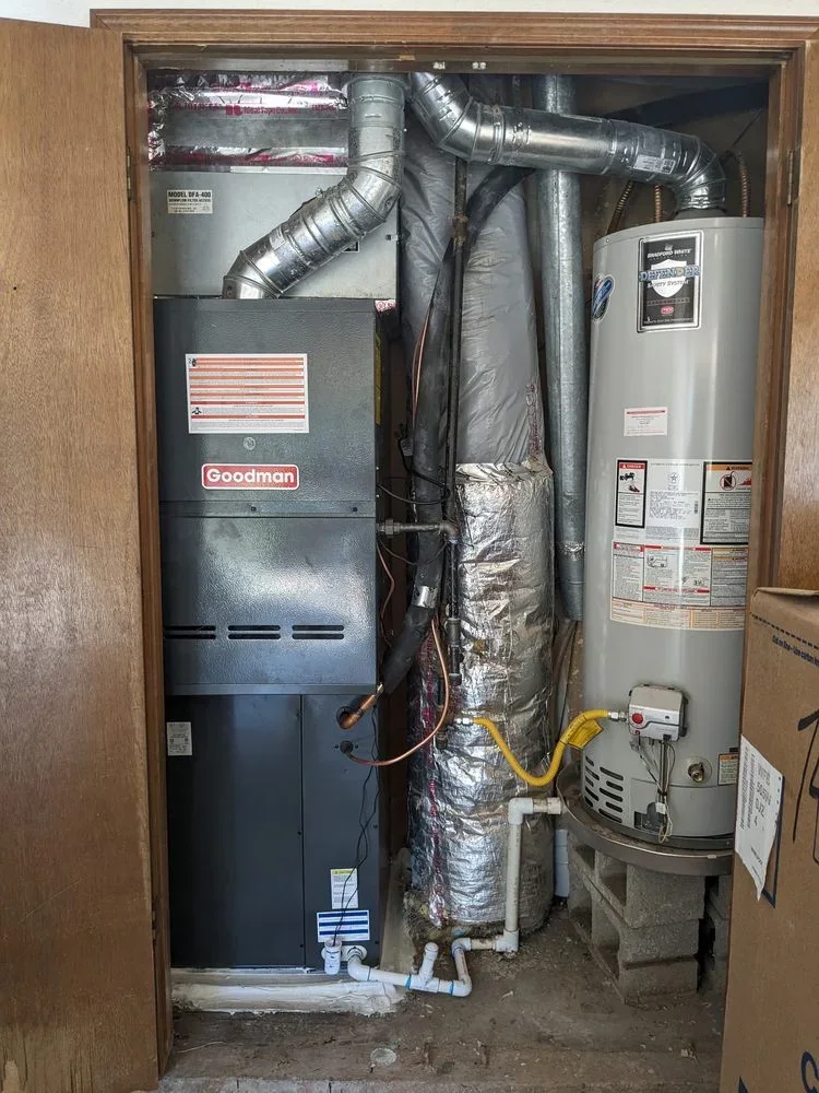 Goodman furnace with connected ductwork beside a water heater in a residential utility closet